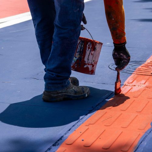 A person paints a red line on a city street, adding vibrant color to the environment.