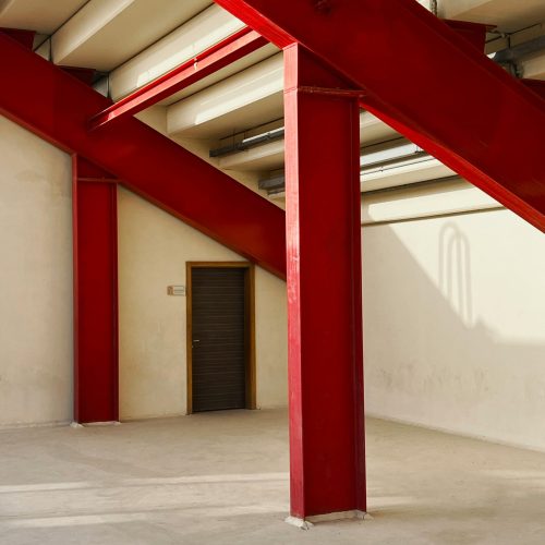 Interior view of a sunlit industrial space with red support beams and a closed door.