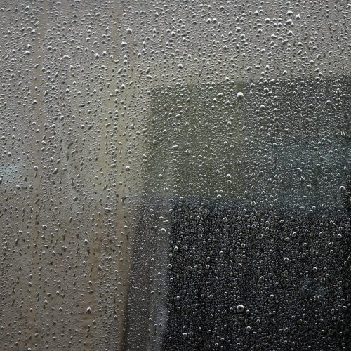 Close-up of a rain-drenched window covered in water droplets, showcasing abstract urban atmosphere.