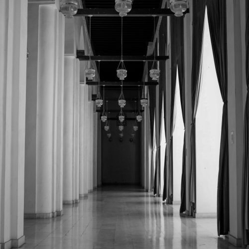 A peaceful corridor inside a historic Cairo mosque, featuring arches and hanging lamps.