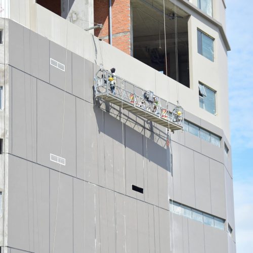 Workers on a suspended platform conducting maintenance on a high-rise building facade.