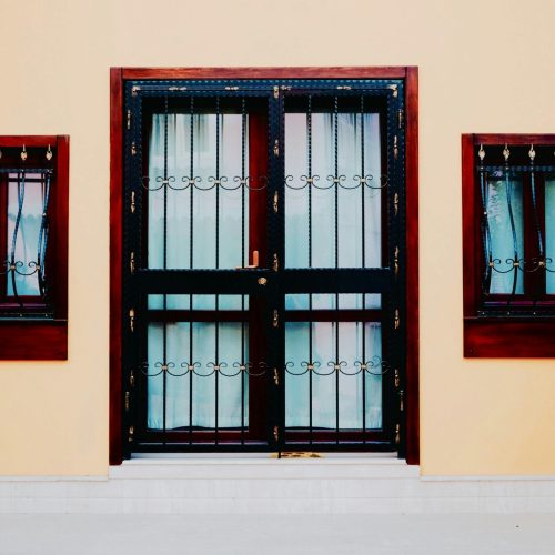 Symmetrical yellow facade with iron grills on doors and windows, reflecting minimal design.