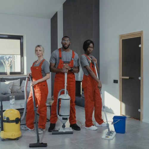Three professional cleaners in uniform inside a modern home with cleaning equipment.